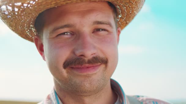 Portrét šťastného bělocha, který se dívá do kamery se zlatým pšeničným polem na pozadí modré oblohy. Koncept zemědělství — Stock video