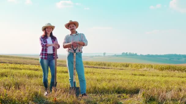 青い空を背景に金色の麦畑を背景にカメラにポーズを取りながら、幸せな男性の白人農家の立っている腕の肖像画は、彼の女性の同僚と交差しました。農業の概念 — ストック動画