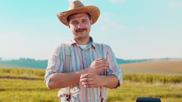 Portret van de blanke boer midden in het tarweveld in het zonlicht en kijkend naar de camera in de blauwe hemel achtergrond — Stockvideo