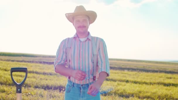 Zdjęcie portretowe białego rolnika stojącego na środku pola pszenicy w słońcu i patrzącego na kamerę w tle niebieskiego nieba — Wideo stockowe