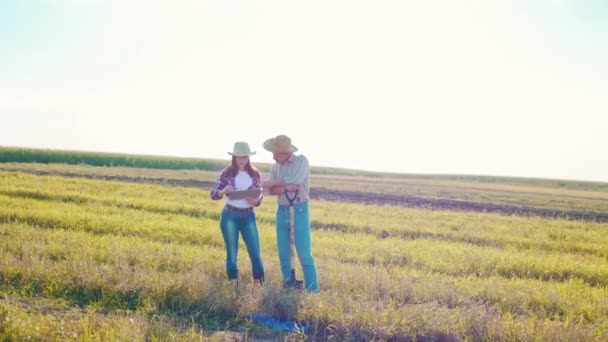 Δύο μηχανικοί αγρότες φορώντας καπέλο εξέταση των φυτών και τον έλεγχο του συστήματος νερού στο πεδίο, ενώ στέκεται και συζητά κατά τη διάρκεια της εξέτασης του tablet. Έννοια βιολογικής γεωργικής δραστηριότητας — Αρχείο Βίντεο