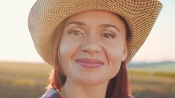 Közelkép a kalapos női gazdáról, amint a kamerába néz egy munkanap után naplementekor. Mezőgazdasági üzleti koncepció — Stock videók