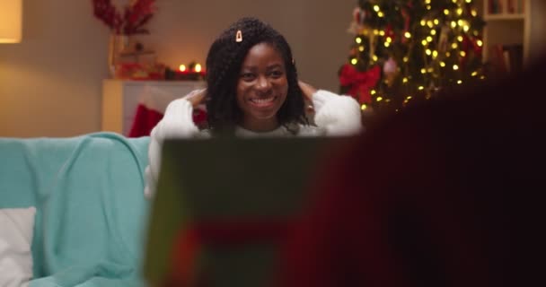 Close up de alegre sorrindo afro-americano mãe bonita sentado em quarto decorado com árvore brilhante recebe presente de xmas de pequeno filho e abraçando o garoto bonito. Criança dando presente à mãe Boas festas — Vídeo de Stock