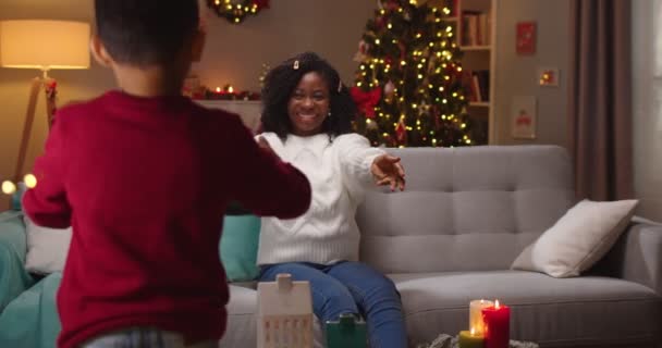 Afrikalı Afrikalı Amerikalı bir çocuğun süslemeli odada annesine Noel hediyesi vermesi. Mutlu anne küçük oğlundan Noel hediyesi alır ve tatlı çocuğunu kucaklar. Aralık tatili — Stok video