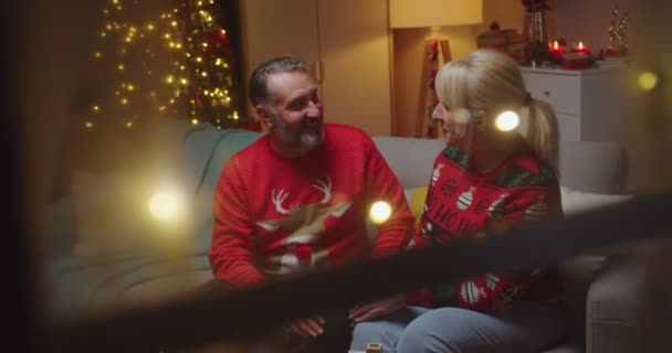 Portrait d'un heureux couple marié âgé caucasien assis à la maison décorée le soir du Nouvel An bavardant et souriant. Joyeux Noël. Saison d'hiver. Concept de famille — Video