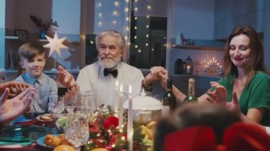 Evdeki Noel yemeğinden önce el ele tutuşup dua etmek. Güzel arkadaşlar yemek masasında oturuyor ve yeni yıl partisinde lezzetli yemekler yiyorlar..