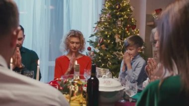 Noel yemeğinden önce evde dua eden sevgili bir aile. Güzel arkadaşlar yemek masasında oturuyor ve yeni yıl partisinde lezzetli yemekler yiyorlar..