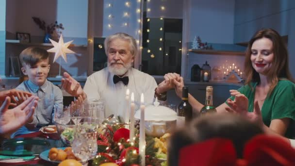 Kochająca rodzina trzymająca się za ręce i modląca przed świąteczną kolacją w domu. Piękni przyjaciele siedzi przy stole z pysznym jedzeniem podczas imprezy sylwestrowej. — Wideo stockowe