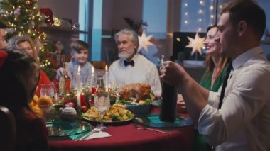 Büyük beyaz bir aile Noel 'i kutluyor, yemek masasında sohbet ediyorlar. Genç ve güzel adam bir şişe şarap açar ve bardakları doldurur..