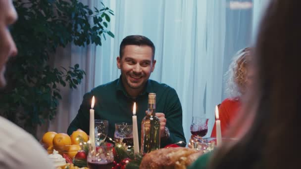 Feliz familia caucásica celebrando la Navidad, charlando en la mesa de la cena. Joven hombre hermoso contando una historia y sonriendo. — Vídeos de Stock