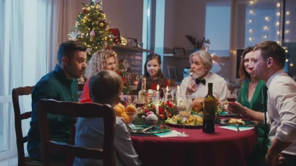 Szczęśliwa, biała rodzina świętuje święta, rozmawia przy stole. Piękni przyjaciele mają świąteczną kolację w domu, jedząc pyszne jedzenie. — Wideo stockowe