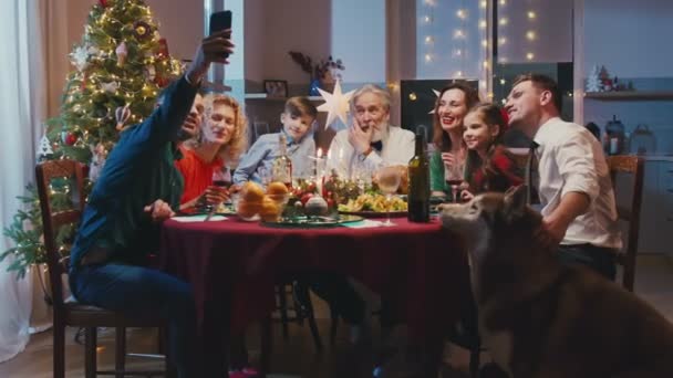 Χαρούμενη καυκάσια οικογένεια γιορτάζει τα Χριστούγεννα, κάθεται στο τραπέζι. Όμορφη χαμογελαστή οικογένεια κάνοντας selfie ή βιντεοκλήση με ένα smartphone σε φίλους ή συγγενείς κατά τη διάρκεια του οικογενειακού γεύματος. — Αρχείο Βίντεο