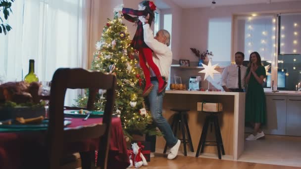 Feliz abuelo y nieta colgando decoraciones en el árbol de Navidad en la fiesta de Navidad o Año Nuevo en casa. Preparación de la celebración de Navidad o vacaciones de invierno. — Vídeo de stock