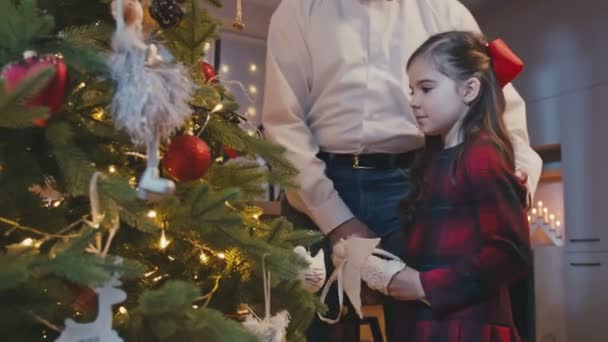 Happy grandfather and granddaughter hanging decorations at Christmas tree at Christmas or New Year party at home. Xmas celebration preparation or winter holidays. — Stock Video