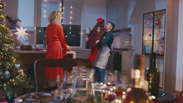 Happy family are cooking and having Christmas dinner together. Mother pepares food and cute little daughter runs to father and they dance. — Stock Video