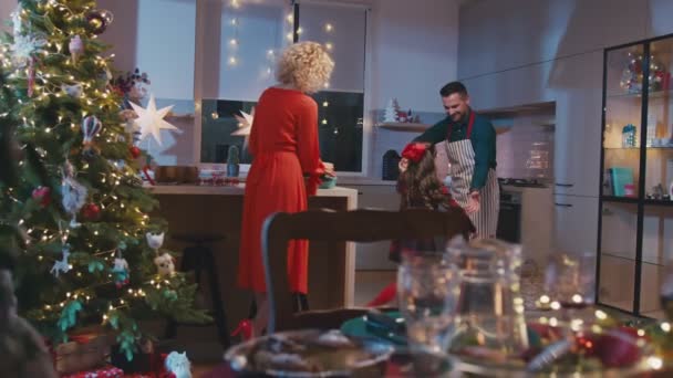 Gelukkige familie koken en hebben kerstdiner samen. Moeder pepares eten en schattig dochtertje rent naar vader en ze dansen. — Stockvideo