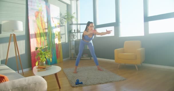 Кавказька вродлива жінка-спортсмен проводить тренування і розігріває м'язи в квартирі в сонячній сучасній кімнаті. Молода жінка займається фізичними вправами вдома. Йога практикується в блокуванні, спортивна концепція — стокове відео