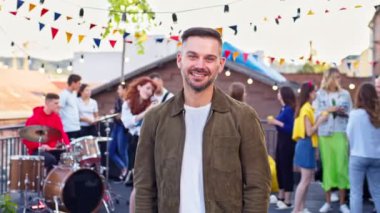 Çatıdaki partide poz veren genç yakışıklı adamın portresi. Çekici erkek kameraya bakıp gülümsüyor. Konser, çatı partisi, bereket konsepti.