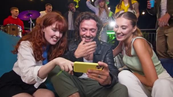 Compagnie de jeunes amis regardant des vidéos drôles sur un téléphone. Les amis de la fête sur le toit s'amusent à écouter le groupe se produire lors d'un concert sur la fête. — Video