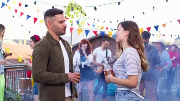 Un homme séduisant sourit et parle à une femme lors d'une fête sur le toit. Beau jeune homme et femme joyeux tiennent et boivent de la bière. — Video