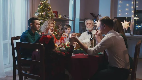 Kochająca rodzina trzymająca się za ręce i modląca przed świąteczną kolacją w domu. Piękni przyjaciele siedzi przy stole z pysznym jedzeniem podczas imprezy sylwestrowej. — Zdjęcie stockowe