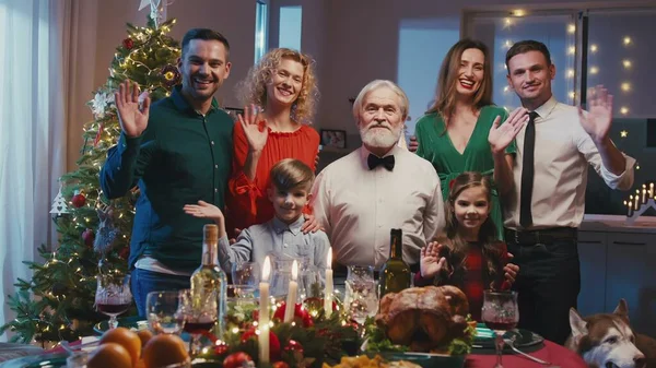 Portrait d'une grande famille heureuse debout près de la table au dîner de Noël, agitant les mains et souriant à la caméra. Belle famille faisant selfie ou appel vidéo à des amis ou des parents. — Photo