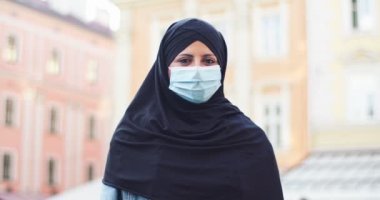 Çekici peçeli kadın müslüman sokakta dikilip kameraya bakıyor. Tıbbi koruyucu maskeli yetişkin bir Arap kadın açık havada tesettür takıyor. Din, insanlar, kültür kavramı.