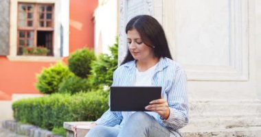 Çekici bayan iş kadını bankta oturuyor ve dijital aletler kullanıyor. Yetişkin bir kadın kahve içiyor, interneti arıyor ve dışarıda çalışıyor. İş, teknoloji konsepti.