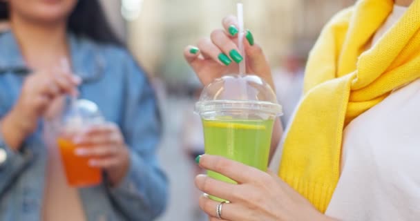 Gros plan des mains féminines tenant la paille et mélangeant les boissons à l'extérieur. Deux femmes parlent et boivent des cocktails de fruits pendant les vacances ensoleillées de l'été. Vacances, amitié, concept de camaraderie. — Video