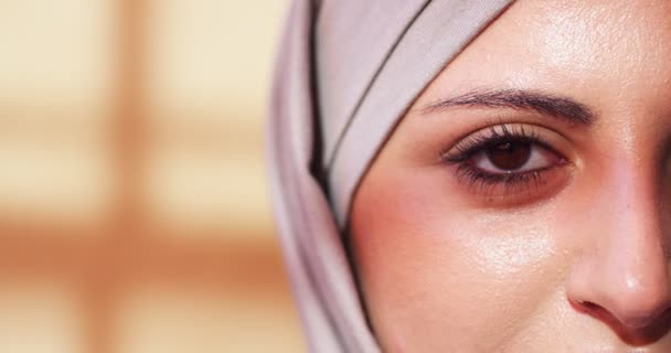 Close up of adult arab female face with brown eyes, veiled head indoors. Beautiful muslim woman wearing purple hijab looking to camera and blinking. Feminity, religion, people concept. — Stock Video