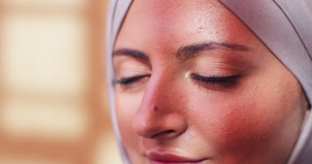 Vista lateral de la cara árabe femenina adul con ojos marrones en el interior. Primer plano de la atractiva mujer musulmana que lleva velo de hijab para cubrir la cabeza, bañándose en la luz del sol. Religión, gente, concepto de belleza. — Vídeos de Stock