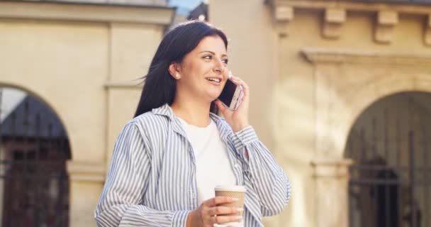 Jolie femme d'affaires marchant dans la rue, appelant un ami et ayant une conversation. Femme arabe adulte parlant au téléphone et buvant du café en ville. Connexion, technologie, concept de communication. — Video