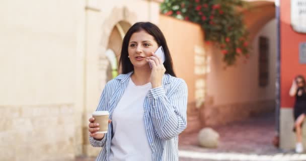 Atractiva mujer caucásica que va a trabajar por la mañana. Mujer de negocios adulta hablando por teléfono, tomando café en la calle. Comunicación, tecnología, concepto de conexión. — Vídeo de stock