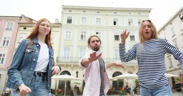 Tres jóvenes femeninos y masculinos se divierten, bailando en la calle de la ciudad. Hombres y mujeres felices disfrutando de la vida, riendo y jugando al aire libre. Juventud, entretenimiento, concepto de adolescencia. — Vídeos de Stock