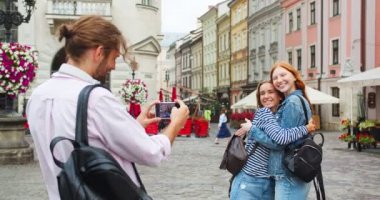 Kafkasyalı turistler akıllı telefondan fotoğraf çekiyorlar. Genç adam kameraya sarılıp gülen güzel kadınları filme alıyor. Teknoloji, seyahat, arkadaşlık konsepti.