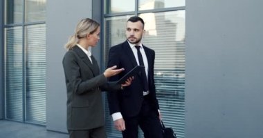 Kafkasyalı iş adamları sokakta birbirleriyle sohbet ediyorlarmış. Kadın dışarıda asistanına tablet ekranda bir şey gösteriyor.