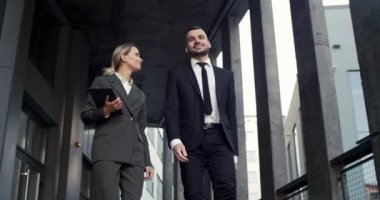 Neşeli ve meşgul, şık, beyaz bir çift iş adamı ve iş kadını şehir merkezinde sokakta yürüyor ve iş konuşuyorlar.