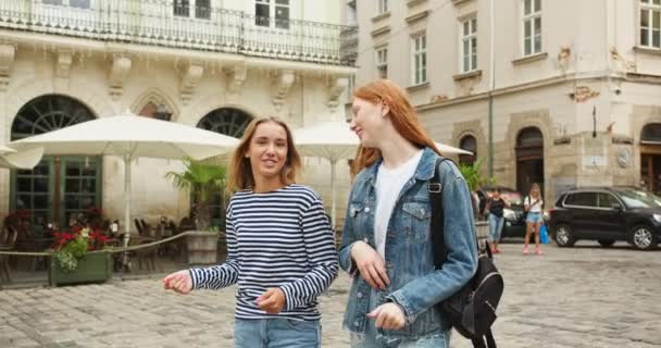 Dos mejores amigas caminando, hablando y mirando a un joven en la calle. Chicas guapas encontrándose con el tipo, saludando, alegrándose de verlo y abrazándose. Amistad, concepto de comunión. — Vídeos de Stock