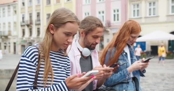 Trois jeunes caucasiens assis sur le banc, ne parlant pas, messages texte. Hommes et femmes adultes utilisant des smartphones, suspendus sur les médias sociaux. Technologie, gadgets, concept de dépendance à Internet. — Video