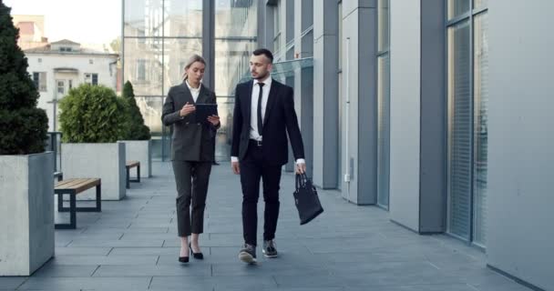 Dos jóvenes caucásicos guapos empresarios caminando juntos en el centro de la ciudad cerca del centro de oficinas y teniendo una agradable charla — Vídeos de Stock