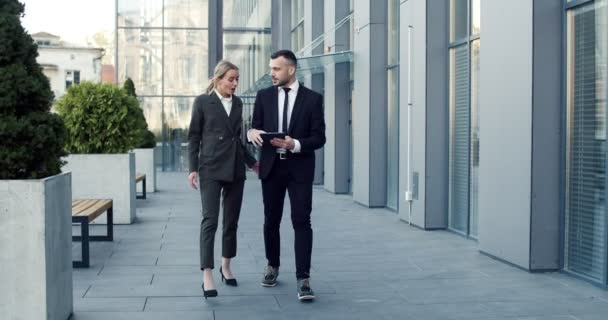 Dos jóvenes caucásicos guapos empresarios caminando juntos en el centro de la ciudad cerca del centro de oficinas y teniendo una agradable charla — Vídeos de Stock