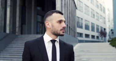 Yakışıklı genç girişimci şehirde sokakta tek başına dikilirken kameraya bakıyor. Kafkas erkek yöneticisinin yakın portresi. İş adamı, akıllı görünüş.