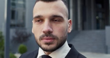 Yakışıklı genç girişimci güneş gözlüklerini çıkarıyor ve şehirde sokakta tek başına dikilirken kameraya bakıyor. Kafkas erkek yöneticisinin yakın portresi. İş adamı, akıllı görünüş.