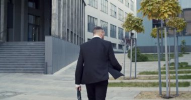 İş merkezinin yakınında açık havada koşarken elinde akıllı telefon tutan meşgul bir erkek müdürün arka görüntüsü. Kafkasyalı işadamı acele et.