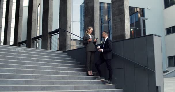 Úspěšný mladý podnikatel a podnikatelka stojí na schodech před velkou městskou kancelářskou budovou a mluví o své práci s šálky kávy jít do rukou — Stock video