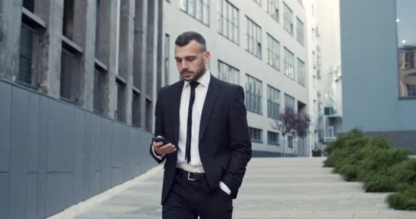 Κοντινό πλάνο πορτρέτο της σοβαρής καυκάσιος αρσενικό επαγγελματικό περπάτημα στην πόλη και τη χρήση smartphone. Όμορφος άντρας μάνατζερ με κινητό στο δρόμο. Έννοια του επιχειρηματία — Αρχείο Βίντεο