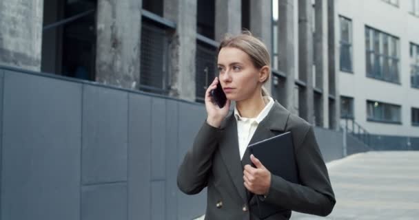 Привлекательная молодая офисная работница в формальной одежде, назначает встречу. Трудолюбивая кавказская деловая женщина разговаривает по телефону. Бизнес, концепция работы — стоковое видео