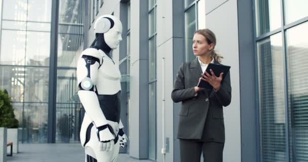 Robô e mulher de negócios parecidos com humanos estão na rua enquanto ela administra dróide com computador tablet. Conceito de novas tecnologias — Vídeo de Stock