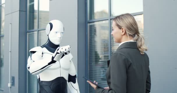 Robot humano y mujer de negocios están moviendo sincronicamente diferentes partes de sus cuerpos mientras se dan cinco entre sí. Mujer manejándolo con Tablet PC — Vídeos de Stock