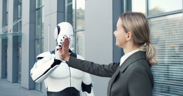 Robot humano y mujer de negocios están moviendo sincronicamente diferentes partes de sus cuerpos mientras se dan cinco entre sí. Mujer manejándolo con Tablet PC — Vídeo de stock